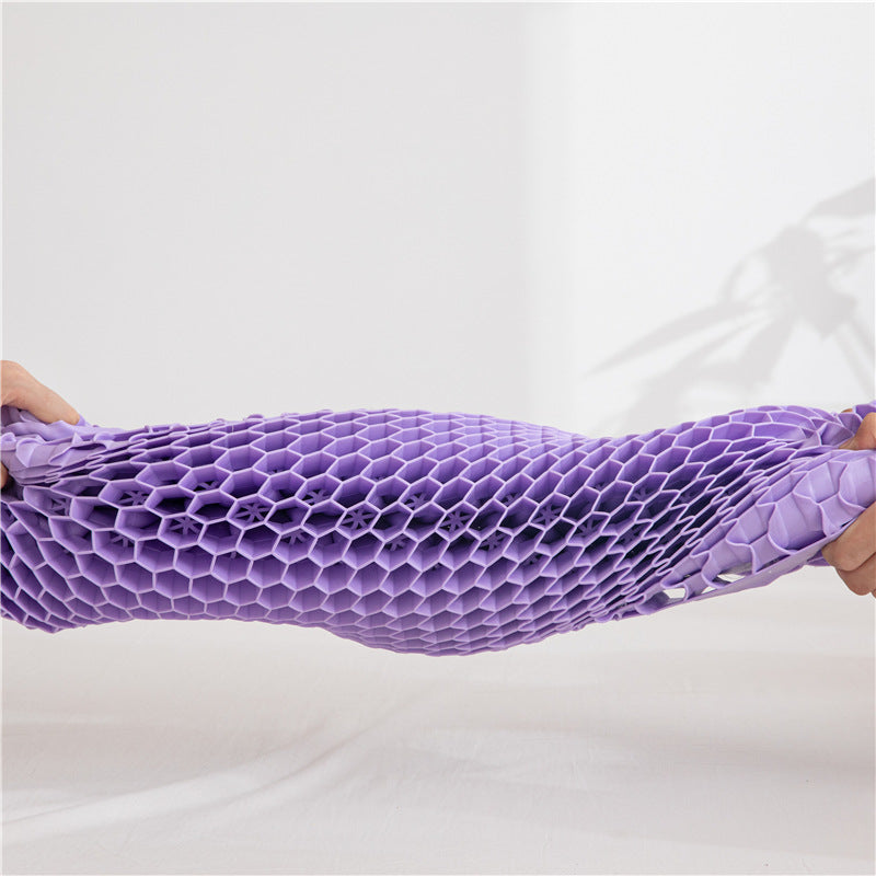 Two hands stretch a honeycomb-patterned, flexible purple material horizontally. The background is plain white with the shadow of a plant on the right, highlighting this cost-effective solution for a zero-pressure sleeping pillow ideal for those with cervical spondylosis. This is the Neck Message Bed Pillow 3D from Cloud Dreams.